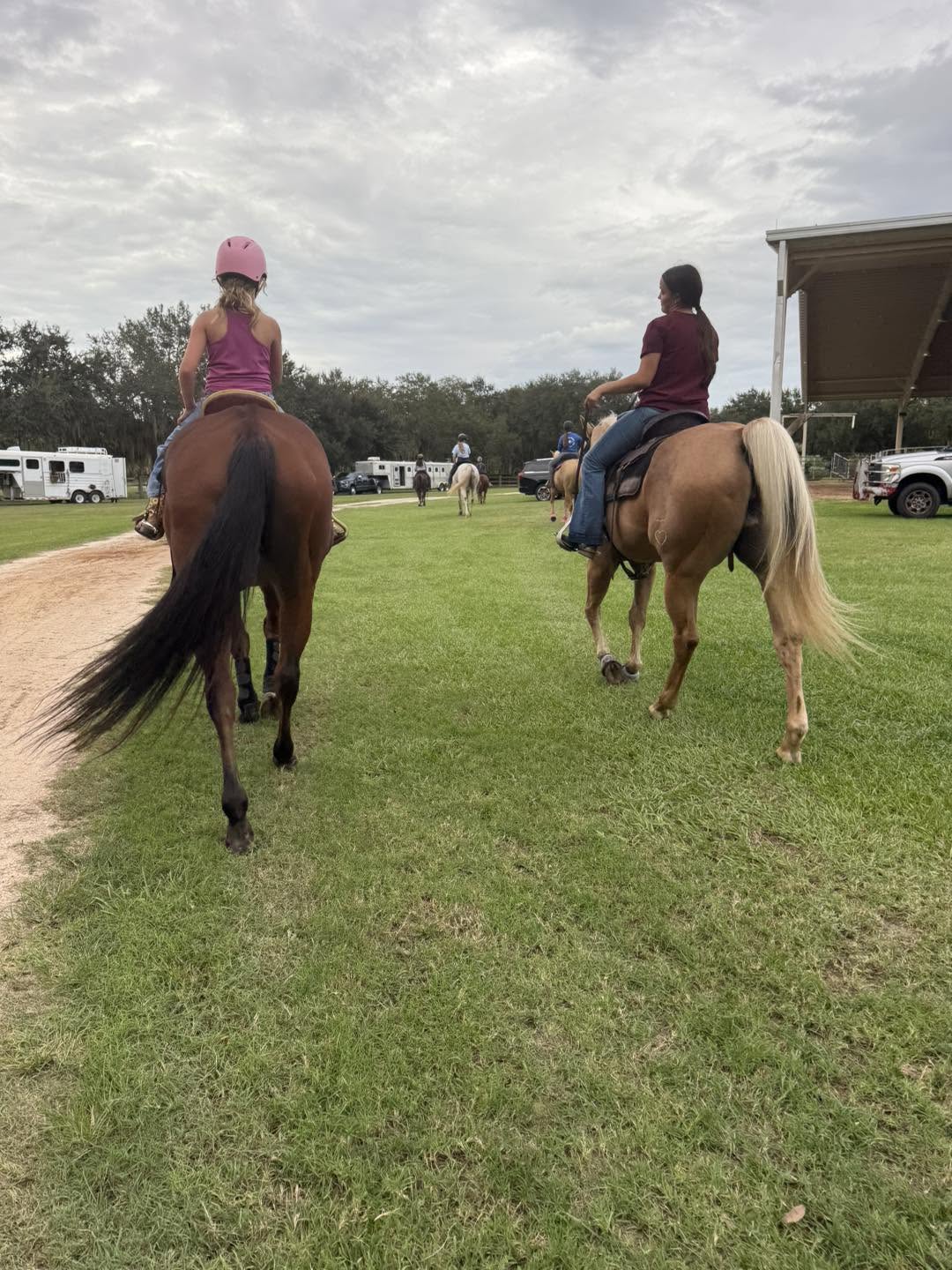 Two riders walking their horses across a grassy field during a group riding lesson.